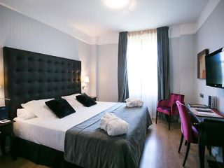 Hotel bedroom with a large bed with a tufted headboard, gray bedding, black accent pillows, and a vibrant pink desk chair