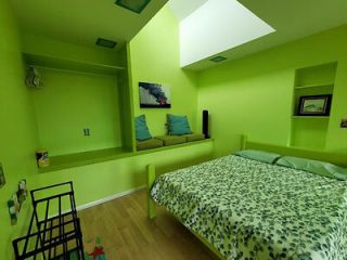 Vibrant green bedroom with large bed covered in a leaf-patterned bedspread, green walls, and a recessed shelf with pillows