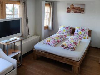 Simple and cozy bedroom with wooden bed frame and colorful floral bedding, with a flat-screen TV on a white stand