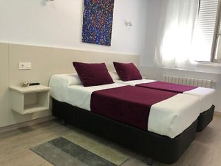 Simple bedroom with a black bed frame, white bedding, and deep red accents, paired with a minimalist nightstand