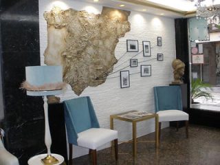 Elegant hotel lobby with a unique gold map wall art, framed pictures, white chairs, and a chic glass-top table