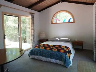 A bright and airy bedroom with a minimalist design, featuring a queen-sized bed with a colorful comforter, and a large arched window