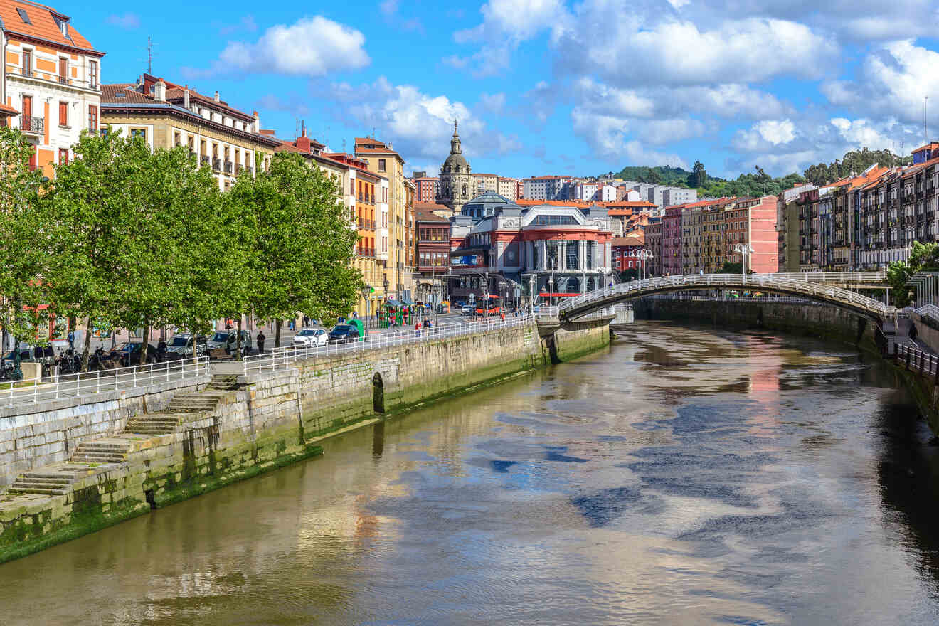 Urban river scene with a stone bridge connecting colorful riverside buildings under a partly cloudy sky