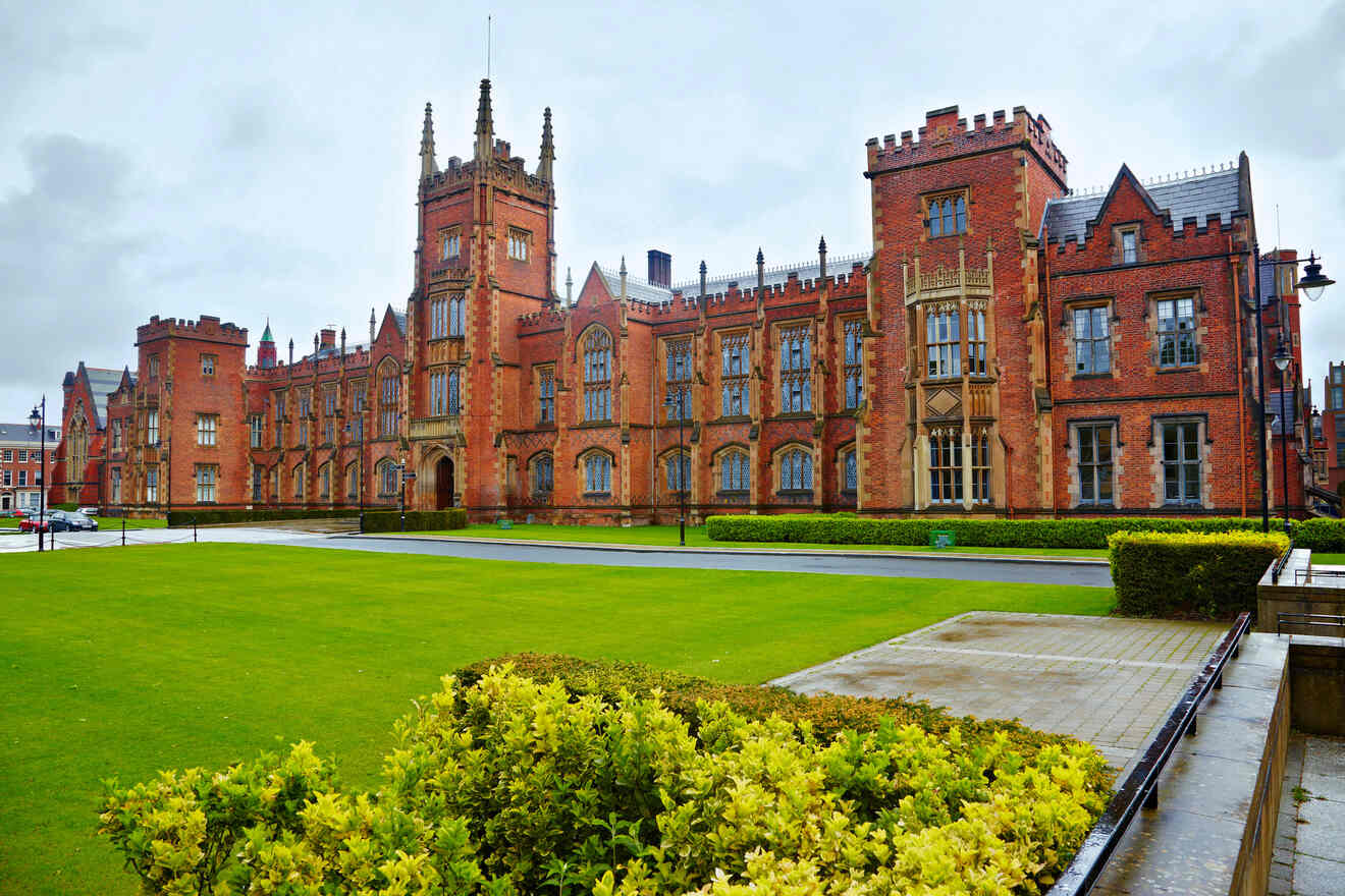 The grandeur of Queen's University Belfast with its historic red brick facade and striking Gothic towers, reflecting on the wet grounds on an overcast day