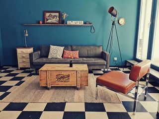 Stylish vintage living room with chequered flooring, a gray couch, and eclectic decor including a wooden crate coffee table and a floor lamp