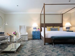 A chic hotel-style bedroom with a four-poster bed, stylish striped armchair, and tasteful floral arrangements