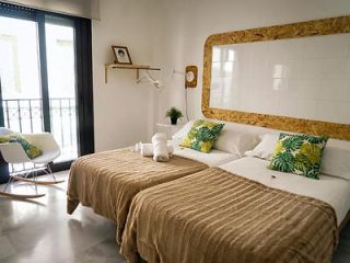 Bedroom with a large mirror framed in natural cork, white bedding with tropical pillows, and a balcony view