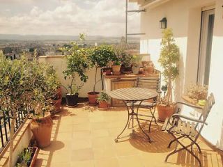 Sunny terrace with potted plants, a tiled floor, and a bistro table set, offering sweeping views of the cityscape