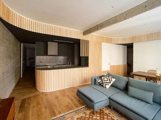 Modern apartment living area with a sleek gray sectional sofa, striped wood paneling, and an open-concept kitchen with contemporary fittings