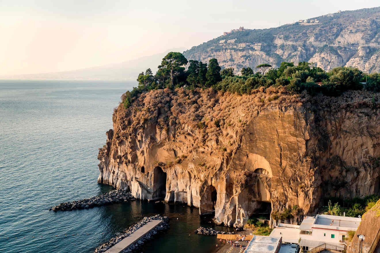 Cliffside view of Sorrento coastline with large caves near the base and buildings on top, sea in the foreground