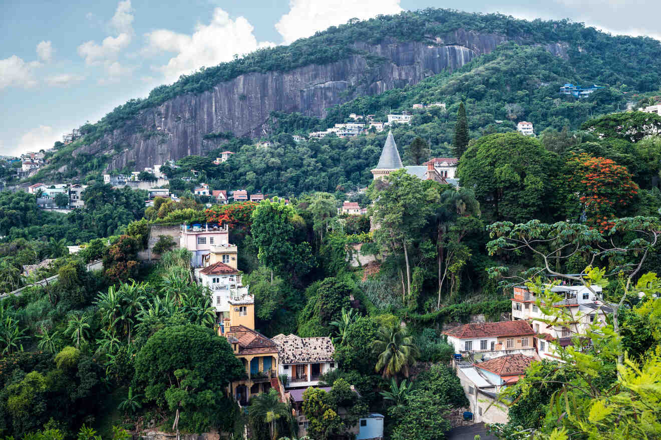 Lush greenery surrounds the quaint, colorful houses nestled at the foot of a rocky mountain in Rio de Janeiro