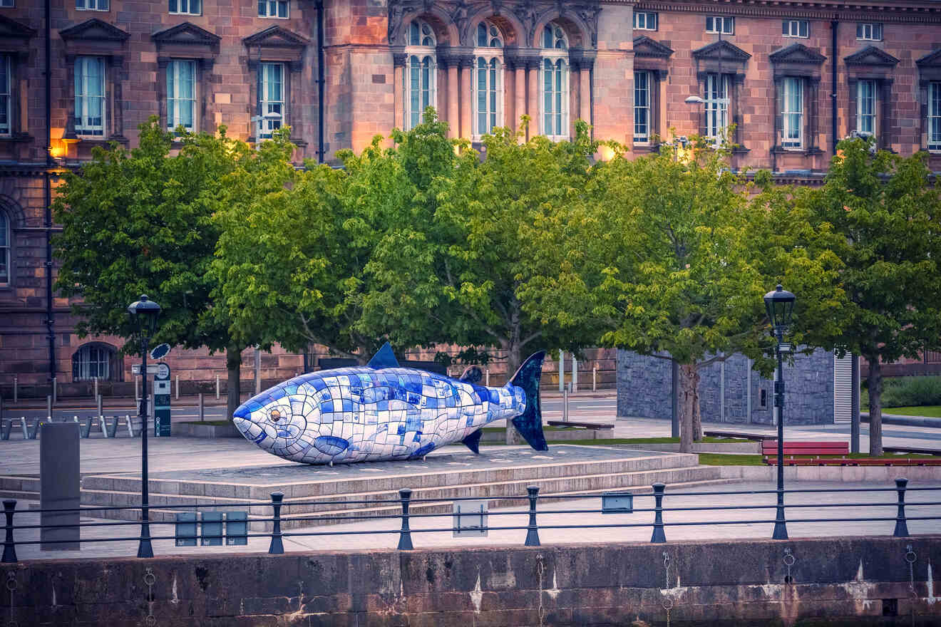 An innovative sculpture of a fish, decorated with blue and white tiles, set in an open plaza with historical architecture in the backdrop