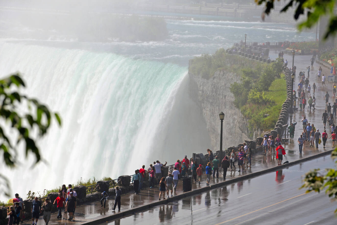 Crowds of tourists wearing raincoats on the mist-covered observation deck at Niagara Falls, with the falls' powerful cascade in the background