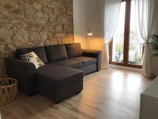 Cozy living room with gray sofa, stone wall, and sheer-curtained windows.