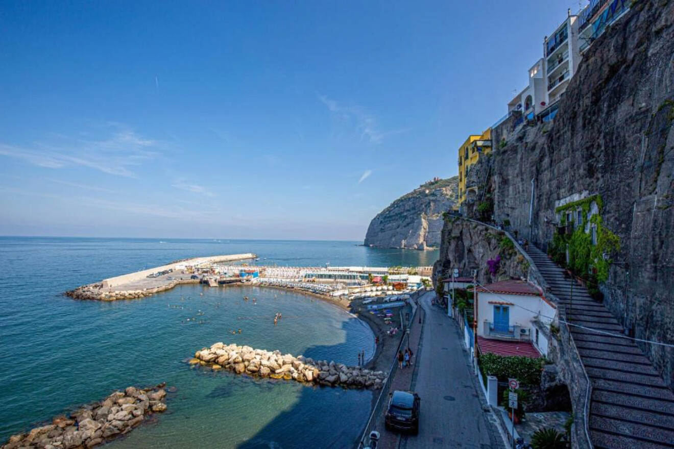 Coastal view of Sorrento with a beach, boats, and a pier, with cliffs and buildings in the background