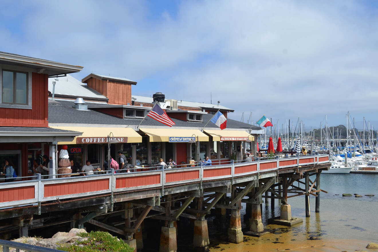 Waterfront dining at a pier restaurant with American and French flags fluttering above, overlooking a marina full of boats on a cloudy da