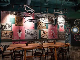 Themed restaurant interior with bicycle decor on the walls and ceilings, and a long communal wooden table with matching chairs