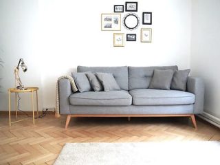 Minimalistic living room with a light gray sofa, white walls decorated with framed pictures, and a small wooden side table with a lamp