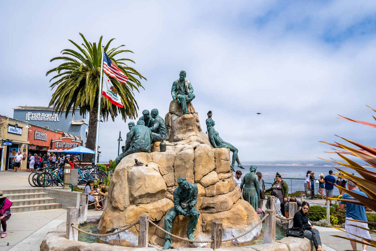 Public monument of historic Cannery Row workers in Monterey, with onlookers and the Fish Hopper restaurant in the background, under a partly cloudy sky