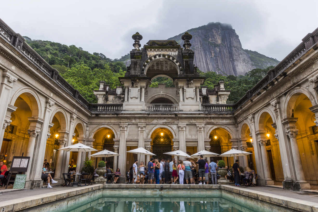 Historic architecture of the Parque Lage with visitors enjoying the café in the foreground and Corcovado Mountain shrouded by clouds in the backdrop