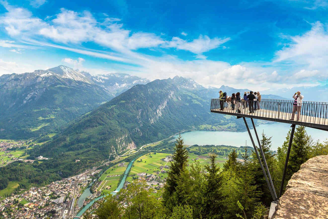 Visitors standing on a cantilevered observation deck extending over a scenic valley with a bird's-eye view of Interlaken and the surrounding Swiss mountains