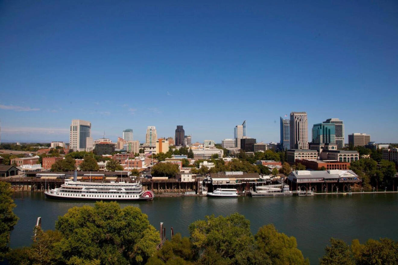 A sweeping view of Sacramento’s skyline seen from the riverfront, featuring the Delta King paddle steamer docked along the riverside.