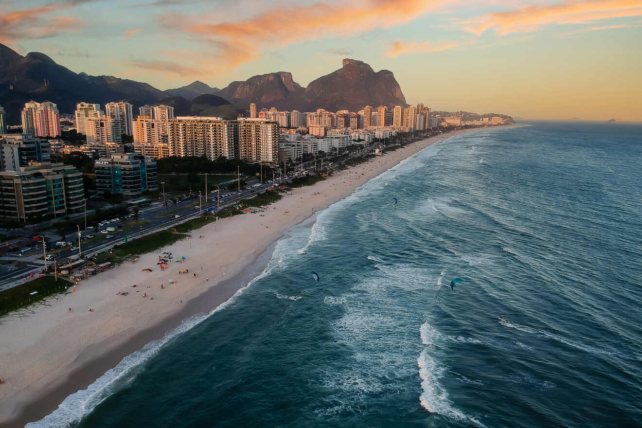 Aerial view of Rio de Janeiro's coastline at sunset, highlighting the curving beach with surfers and the city's skyscrapers