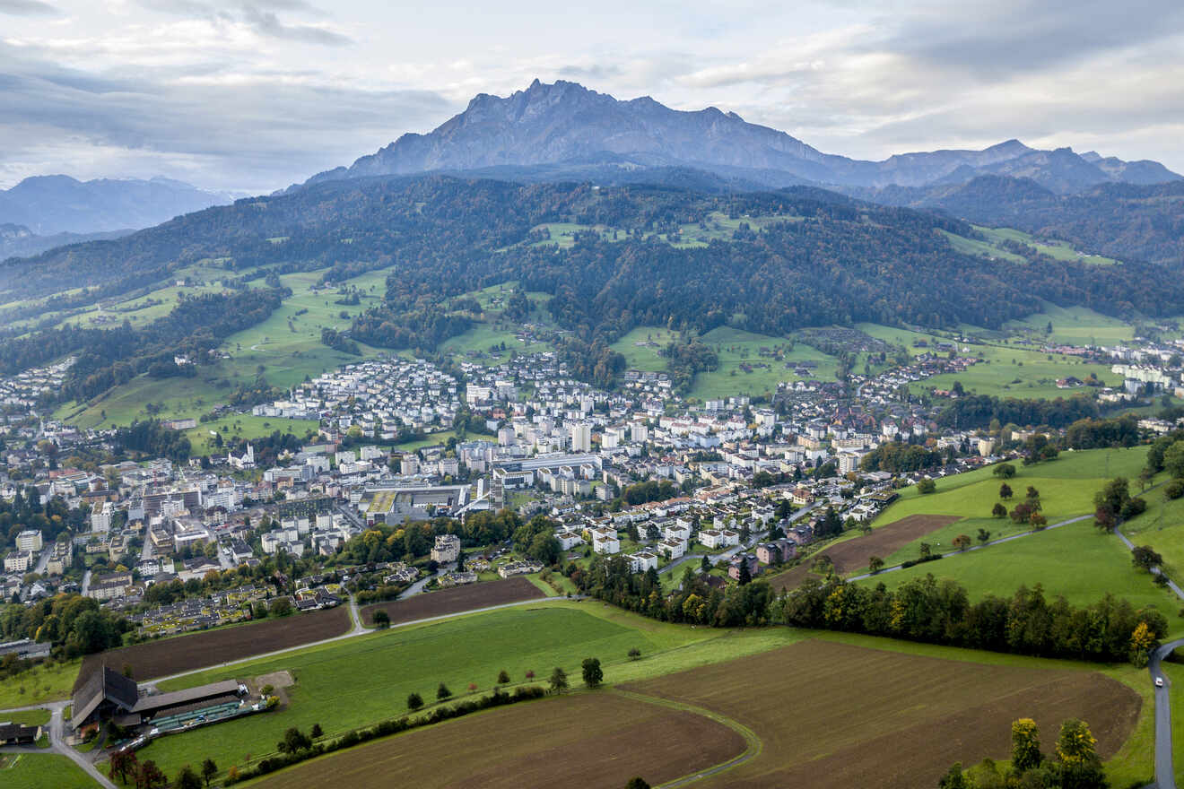 Panoramic view of a Swiss town with buildings spread across a lush green valley, framed by mountains and a cloudy sky