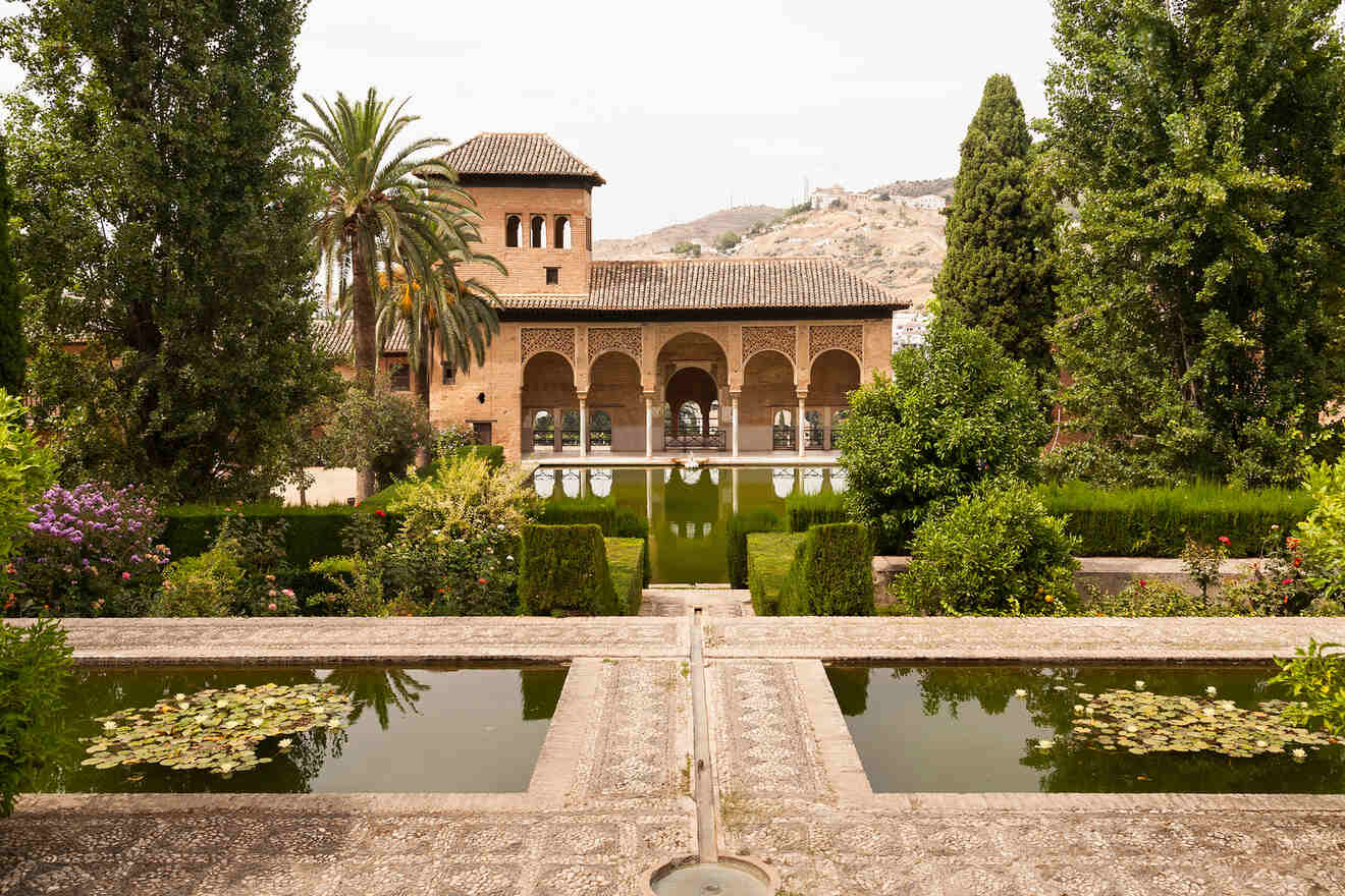 Lush gardens of the Alhambra with reflecting pools, vibrant flora, and the historic architecture of the Palacio del Partal in the background