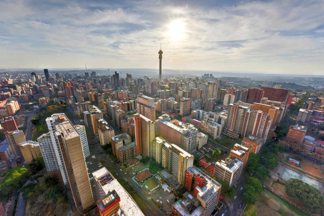 A panoramic aerial view of Johannesburg with a focus on Hillbrow Tower amidst the urban skyline under a sunlit sky