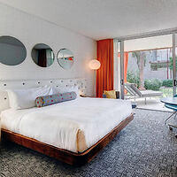 A modern hotel room with a king-sized bed, circular mirrors on the wall, and a patio door leading outside.