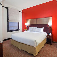 A cozy hotel room with a red accent wall, white bedding, and warm lighting.