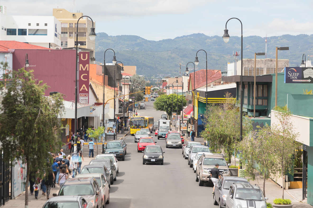 A bustling street in San José, Costa Rica, lined with cars and people, with mountains in the background.