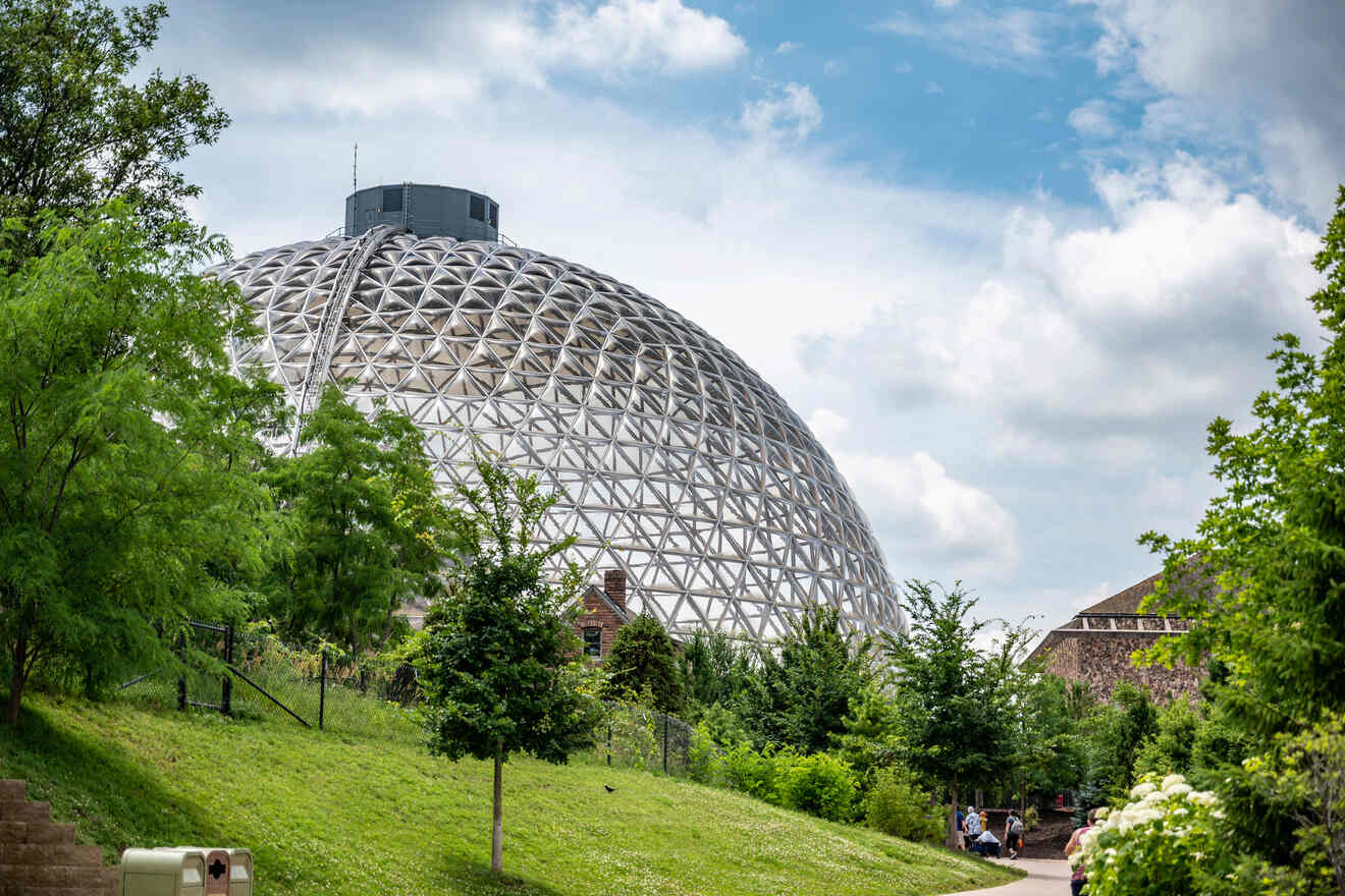 A large geodesic dome of the Omaha Zoo surrounded by green trees and grassy areas.