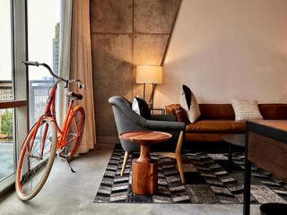 Urban-chic interior with a vintage orange bicycle next to a modern gray armchair and a wooden side table over a patterned rug
