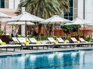 Poolside loungers under white umbrellas by a tranquil pool with palm trees in the background