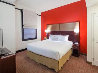A cozy hotel room with a red accent wall, white bedding, and warm lighting.