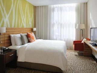 Modern hotel room with a large bed, white and orange decor, and a green patterned wall.
