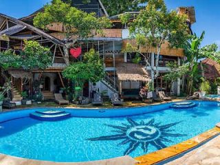 Unique hotel pool with a blue sun motif at the bottom, surrounded by rustic wooden architecture and lush greenery, creating a tranquil oasis