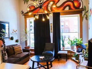 Cozy and artistic urban living space with vibrant wall art, eclectic furnishings, and ample greenery in a well-lit room with large windows