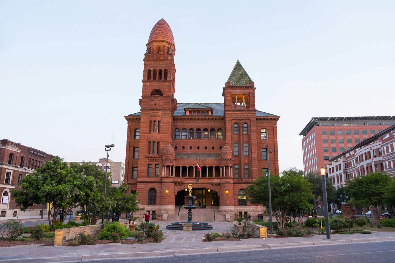 Historic red sandstone courthouse building in San Antonio, Texas, at dusk with a clear sky and surrounding greenery