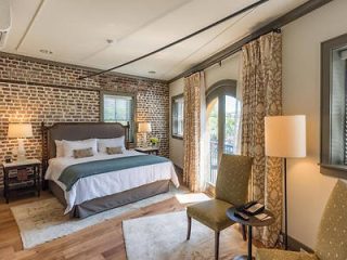 Cozy bedroom interior with exposed brick walls, a plush queen bed with gray and white bedding, elegant draperies, and tasteful décor 