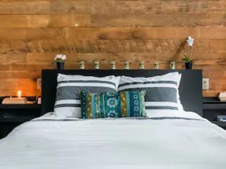 Contemporary bedroom with a wood plank accent wall, a bed adorned with patterned pillows, and small white vases on bedside tables