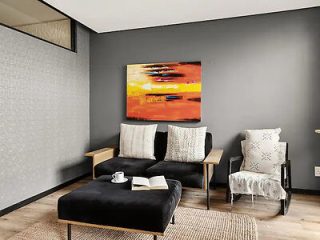 A cozy lounge area with a black ottoman, two chairs, a sofa, and a striking orange abstract painting on a gray wall