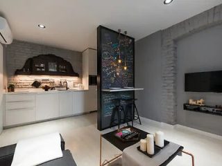 A modern apartment with a compact kitchen, a wall-mounted blackboard with colorful notes and a small bar, and a living area featuring a TV and minimalistic decor.
