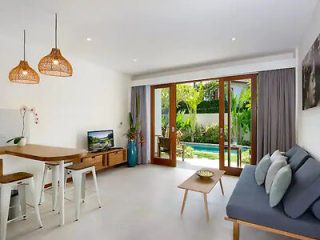 Bright and airy dining area in a contemporary villa, with large glass doors that lead to a lush garden, furnished with a wooden table, modern chairs, and stylish hanging lamps
