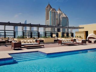 Rooftop pool area with chic lounge furniture, overlooking urban skyscrapers under a clear sky.