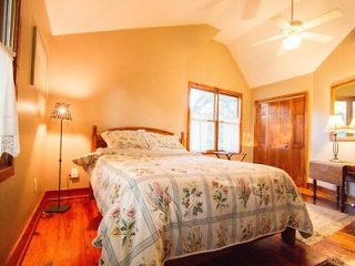 Comfortable bedroom with wooden floors, a queen-sized bed covered in floral linen, a standing lamp, and a ceiling fan