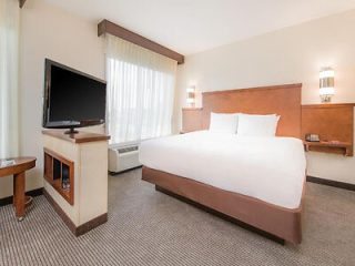 A contemporary hotel room with a king-sized bed, crisp white linens, wooden headboard, and modern amenities including a flat-screen TV and a warmly lit bedside lamp