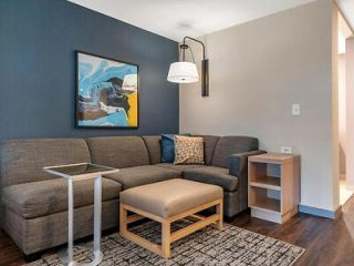 Modern living room with a gray L-shaped sofa, a tan ottoman, a side table, and abstract wall art